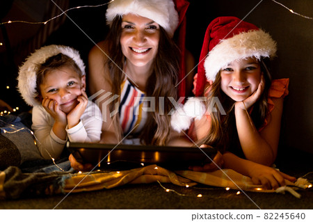 Happy caucasian mother, daughter and son wearing santa hats, using tablet at christmas time 82245640