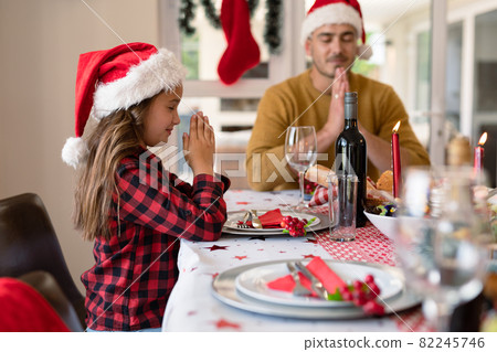 Caucasian daughter and father wearing santa hats praying at christmas table Caucasian daughter and father wearing santa hats praying at christmas table 82245746