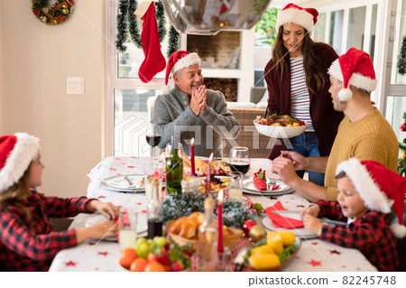 Caucasian multi generation family wearing santa hats having christmas meal Caucasian multi generation family wearing santa hats having christmas meal 82245748