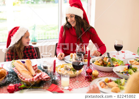 Happymother and daughter wearing santa hats sitting at christmas table 82245802