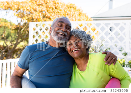 Smiling african american senior couple holding yoga mats in garden and looking at camera Smiling african american senior couple holding yoga mats in garden and looking at camera 82245996
