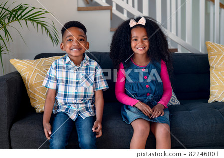 Happy african american siblings sitting on sofa and looking at camera 82246001