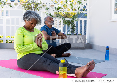 Focused african american senior couple practicing yoga on mat in garden Focused african american senior couple practicing yoga on mat in garden 82246002