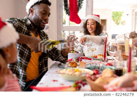 Happy african american father pouring wine to glass at christmas table Happy african american father pouring wine to glass at christmas table 82246279
