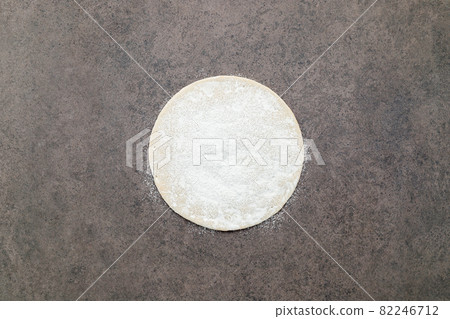 Thin homemade pizza dough with scattered wheat flour on dark concrete background. 82246712