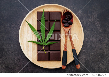 Food conceptual image of  cannabis leaf  with dark chocolate and fork on dark concrete background. 82246724