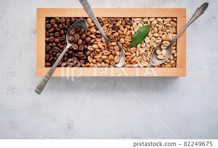 Green and brown decaf unroasted and dark roasted coffee beans in wooden box with scoops setup on white concrete background. with scoons setup on white concrete background. Green and brown decaf unroasted and dark roasted coffee beans in wooden box with scoops setup on white concrete background. with scoons setup on white concrete background. 82249675