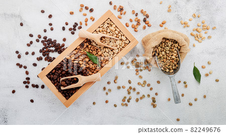 Green and brown decaf unroasted and dark roasted coffee beans in wooden box with scoops setup on white concrete background. Green and brown decaf unroasted and dark roasted coffee beans in wooden box with scoops setup on white concrete background. 82249676
