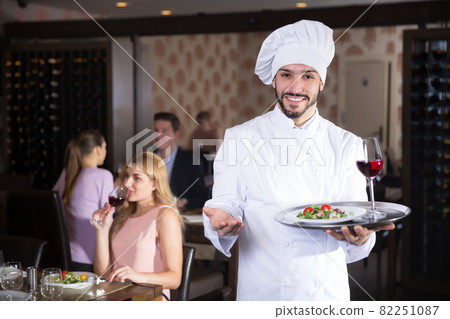 Glad chef with serving tray meeting guests 82251087