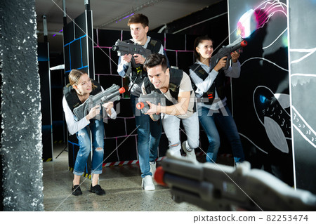 Cheerful Laser tag players young mens and womens playing in teams in dark laser tag station Cheerful Laser tag players young mens and womens playing in teams in dark laser tag station 82253474
