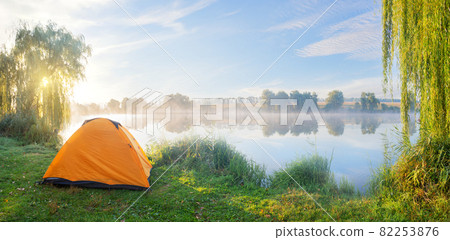 Foggy lake shore with orange tent in morning sun 82253876