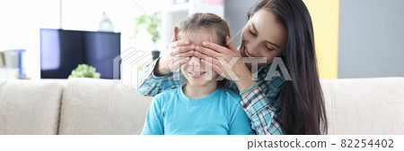 Young mother closes her daughter eyes and gives her gift 82254402