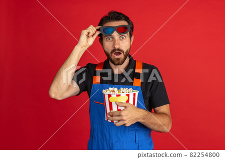 Surprised young bearded man, male auto mechanic or fitter wearing blue work dungarees isolated over red studio background. Concept of facial emotions Surprised young bearded man, male auto mechanic or fitter wearing blue work dungarees isolated over red studio background. Concept of facial emotions 82254800
