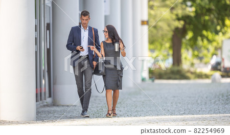 Two office workers walk to work discussing news on the mobile phone 82254969