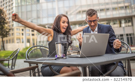 Male and female coworkers showing thrilled enthusiasm over successful deal just done on a laptop in fron of them outdoors in the city Male and female coworkers showing thrilled enthusiasm over successful deal just done on a laptop in fron of them outdoors in the city 82254970