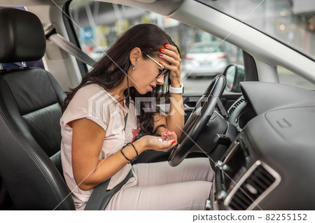 Woman in dispair holds her head sitting on driver's seat with a handfull of pills in her other hand Woman in dispair holds her head sitting on driver's seat with a handfull of pills in her other hand 82255152