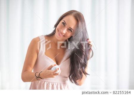 Beautiful brunette in pink dress with cleavage sprays her hair with hair spray, smiling 82255164