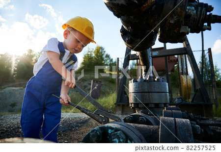 Caucasian blonde boy with instrument fixing drilling rig during time for learning at petroleum station in nature environment, young man in professional uniform studying engineering at oil platform Caucasian blonde boy with instrument fixing drilling rig during time for learning at petroleum station in nature environment, young man in professional uniform studying engineering at oil platform 82257525
