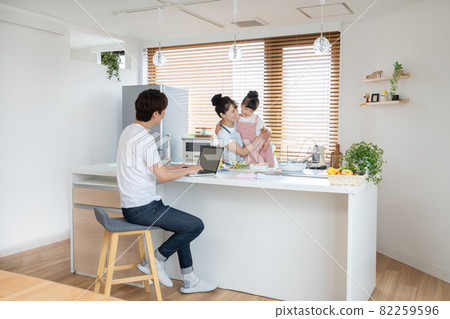 Elementary school girl and mom making lunch in the kitchen. Daddy working on a computer 82259596