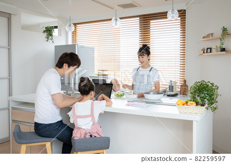 Mom making lunch in the kitchen and dad and elementary school girl looking at a computer Mom making lunch in the kitchen and dad and elementary school girl looking at a computer 82259597