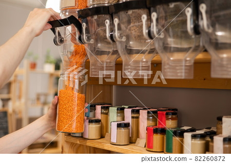 A man fills a jar with red lentils. Selling bulk goods by weight in an eco store. Trade concept without plastic packaging A man fills a jar with red lentils. Selling bulk goods by weight in an eco store. Trade concept without plastic packaging 82260872