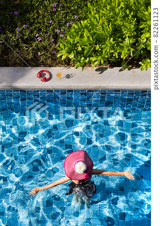 Woman wearing big hat walking in pool. 82261123