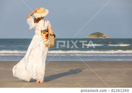 Woman wearing hat and holding bag on beach Woman wearing hat and holding bag on beach 82261269