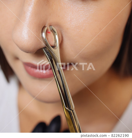 Closeup of a young woman's visage with piercing hanging from her nose. 82262190