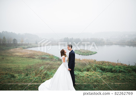 Romantic, fairytale, happy newlywed couple hugging and kissing in a park, trees in background Romantic, fairytale, happy newlywed couple hugging and kissing in a park, trees in background 82262769