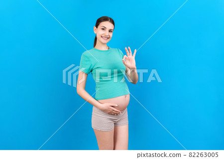 positive pregnant woman showing okay gesture against her belly at colored background. Easy and happy pregnancy. Copy space 82263005