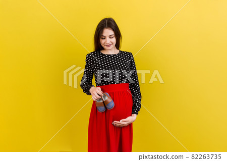 Happy pregnant woman showing small boots for a baby boy at Colored background. Future mother is waiting for a child. Copy space 82263735