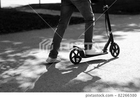 Young boy legs with jeans riding two wheeled push scooter. scooter black and white image. white shoes on legs. 82266380