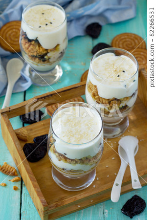 Vegan Dessert with whipped cream, nuts, oatmeal, prunes and sesame in glass glasses on a wooden rustic table. Vegan Dessert with whipped cream, nuts, oatmeal, prunes and sesame in glass glasses on a wooden rustic table. 82266531