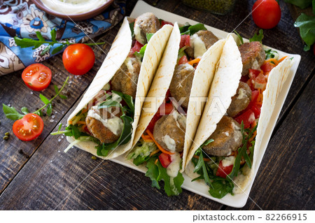Delicious fresh homemade tortilla wrap with falafel and fresh salad on the table. Vegan tacos. Vegetarian healthy food. Delicious fresh homemade tortilla wrap with falafel and fresh salad on the table. Vegan tacos. Vegetarian healthy food. 82266915