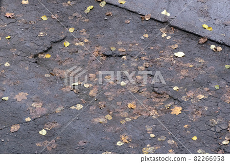 Pits in the asphalt and yellow autumn leaves. The old road. Poor road surface. Top view. 82266958