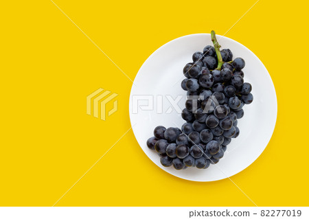 Fresh black grapes in white plate on yellow background. Fresh black grapes in white plate on yellow background. 82277019