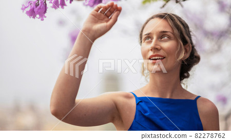Caucasian woman in blue dress touching pink tree flowers in Barcelona 82278762
