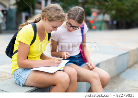 Two happy teenage students studying homework with copybook sitting on parapet outside Two happy teenage students studying homework with copybook sitting on parapet outside 82279025