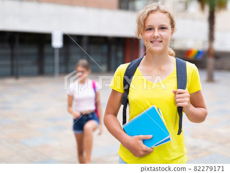 Girl with copybooks standing beside school building 82279171