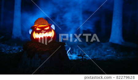 Creepy carved pumpkin for Halloween with blue smoke in the forest. 82279628