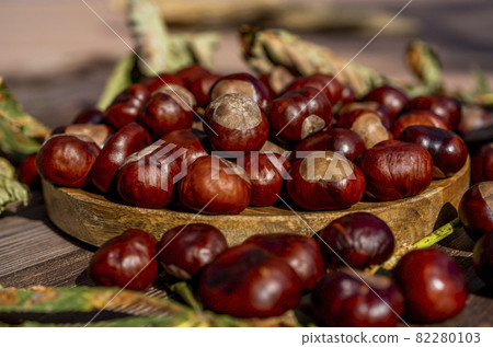 Chestnuts in a plate with dry leaves on a brown wooden table. Autumn still life with bright horse chestnuts on wooden background Chestnuts in a plate with dry leaves on a brown wooden table. Autumn still life with bright horse chestnuts on wooden background 82280103