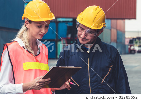 Industrial worker works with co-worker at overseas shipping container yard Industrial worker works with co-worker at overseas shipping container yard 82285652
