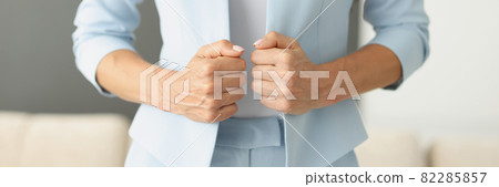 Woman in blue suit holding edges of her jacket with her hands closeup Woman in blue suit holding edges of her jacket with her hands closeup 82285857