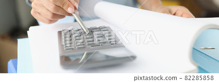 Woman leafing through folder with documents and looking at calculator closeup Woman leafing through folder with documents and looking at calculator closeup 82285858