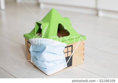 quarantine coronovirus concept. a toy house in a medical mask stands on the floor of the house. quarantine coronovirus concept. a toy house in a medical mask stands on the floor of the house. 82286109