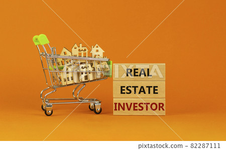 Real estate investor symbol. Wooden blocks, words 'Real estate investor' on beautiful orange background. Shopping cart with miniature wooden houses. Business, Real estate investor concept. Copy space. 82287111