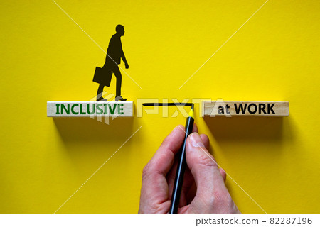 Inclusive at work symbol. Wooden blocks with words 'Inclusive at work' on beautiful yellow background. Businessman hand. Businessman icon. Business, inclusive at work concept. Copy space. Inclusive at work symbol. Wooden blocks with words 'Inclusive at work' on beautiful yellow background. Businessman hand. Businessman icon. Business, inclusive at work concept. Copy space. 82287196