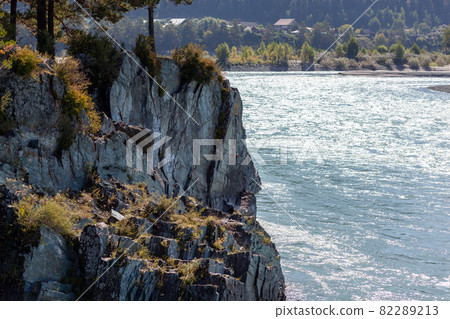 A fast-flowing wide and full-flowing mountain river. Large rocks stick out of the water. Big mountain river Katun, turquoise color, in the Altai Mountains, Altai Republic. A fast-flowing wide and full-flowing mountain river. Large rocks stick out of the water. Big mountain river Katun, turquoise color, in the Altai Mountains, Altai Republic. 82289213