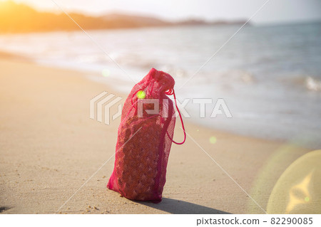 Mesh shopping bag with fruits stands on the sandy beach of the sea on a sunny day. ecology of the oceans concept 82290085