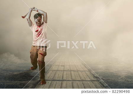 Scary zombie with blood and wound on his body holding sickle walking Scary zombie with blood and wound on his body holding sickle walking 82290498